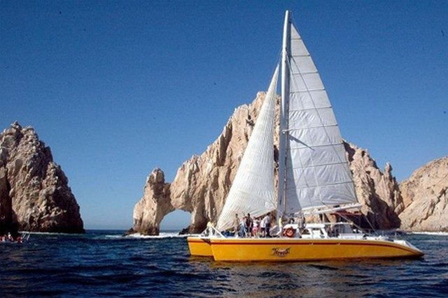 Sailing catamaran with yellow hulls in front of El Arco